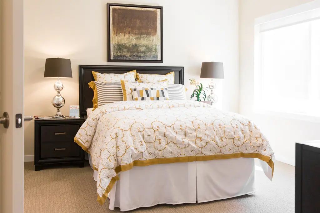 A well-decorated bedroom featuring a luxurious bed with patterned bedding, flanked by matching lamps on dark nightstands, and adorned with wall art.