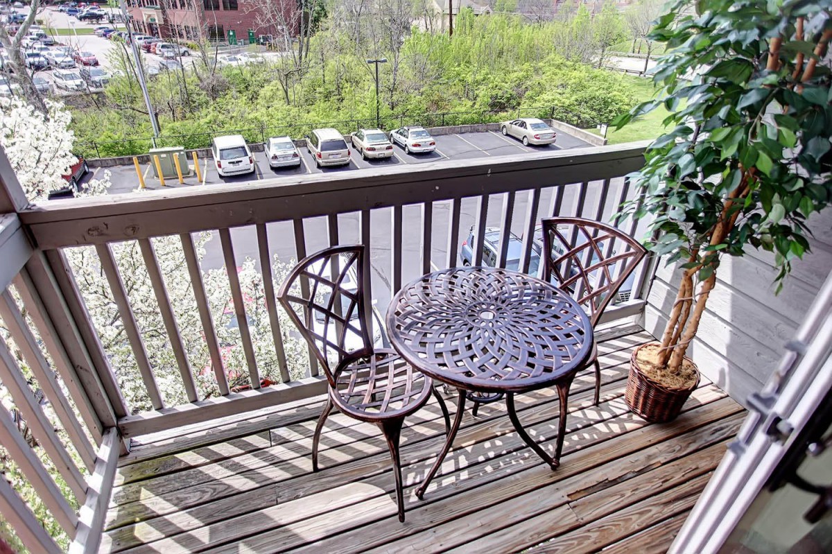 A cozy balcony with a metal table and chairs overlooking a parking lot and greenery.