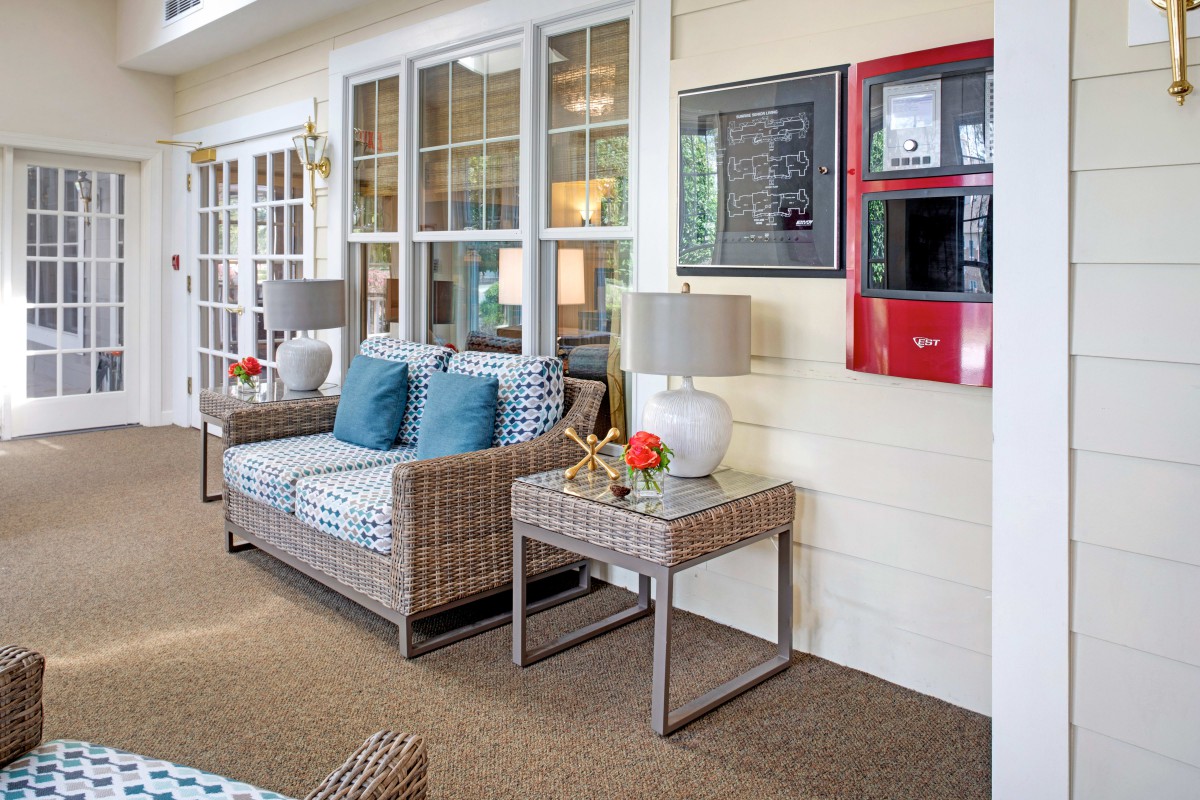 A cozy living room area featuring rattan furniture, a sofa with blue cushions, two side tables, and decorative lamps.