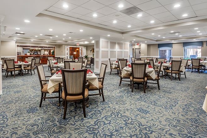 A well-lit dining area with neatly arranged tables and chairs on a patterned carpet.