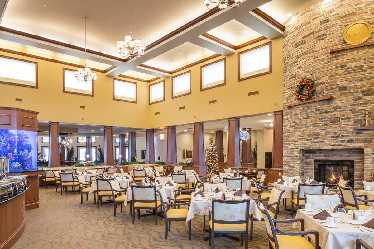 A spacious indoor dining area with neatly arranged tables and chairs, illuminated by chandeliers.