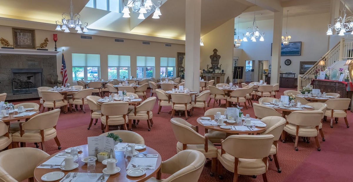 A spacious and elegantly decorated dining room with neatly arranged tables and chairs, well-lit by overhead lights.