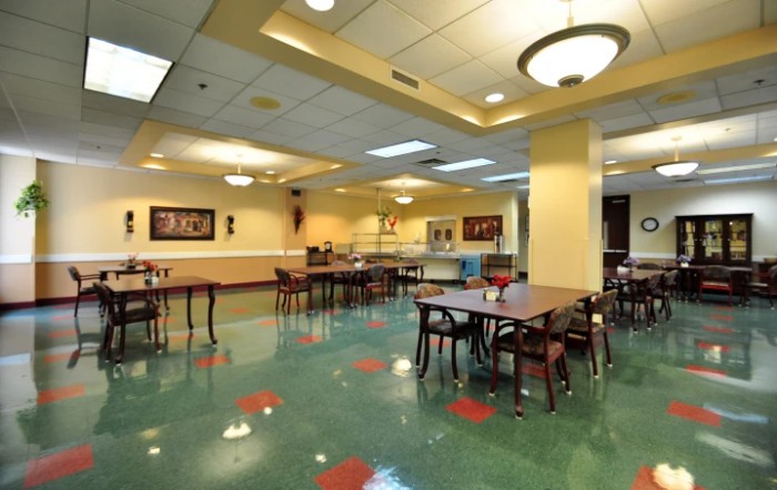 An empty cafeteria with neatly arranged tables and chairs, lit by overhead lights.
