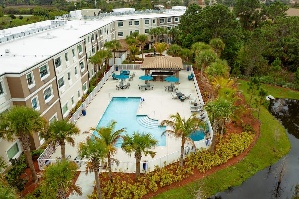 Aerial view of an apartment complex featuring a swimming pool surrounded by palm trees and lush landscaping.