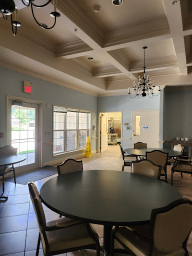A bright and inviting community dining area featuring round tables and a chandelier under a coffered ceiling.