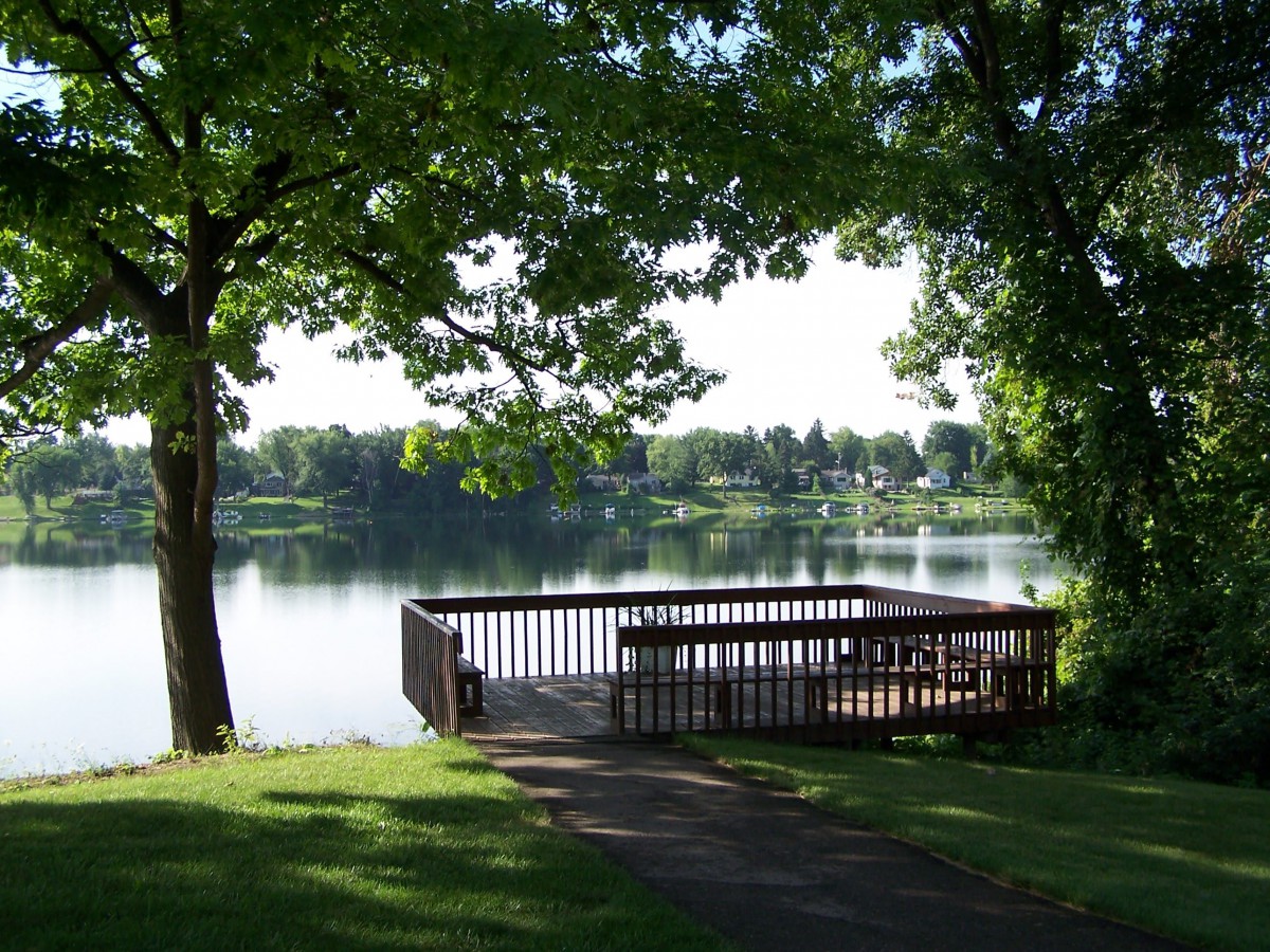 A peaceful lakeside view with a wooden dock surrounded by lush trees.