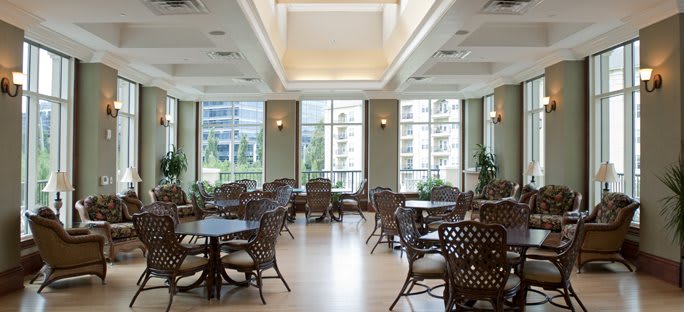A spacious dining area with multiple tables and chairs, well-lit by natural light streaming through large windows.