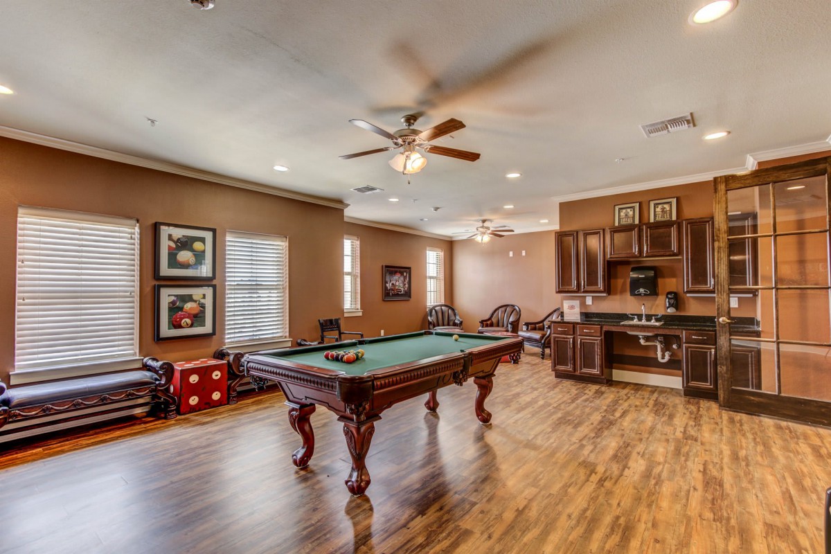 A cozy game room featuring a billiards table, complete with wood flooring and a kitchen area.