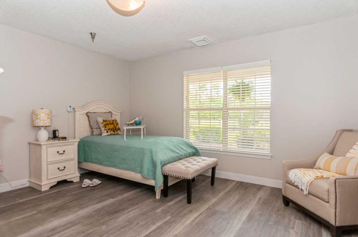 A cozy bedroom featuring a single bed with green bedding, a nightstand, and a large window letting in natural light.