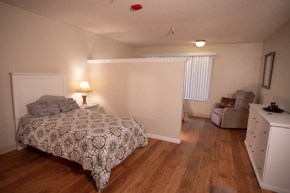 A cozy bedroom with a bed, lamp, and wooden flooring.