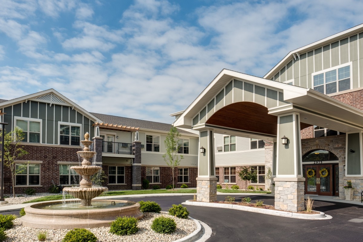 A modern building with a driveway entrance and a fountain under a partly cloudy sky.