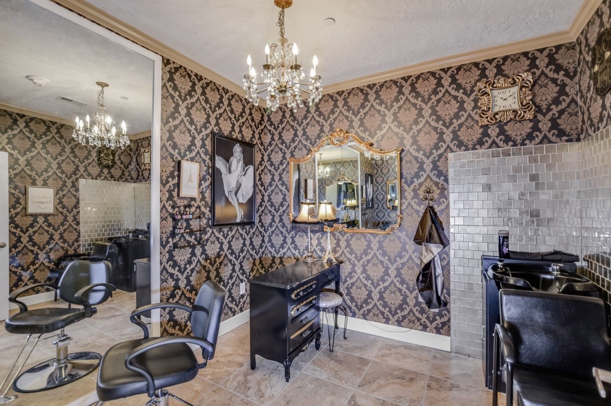 A stylish salon interior with vintage wallpaper, a chandelier, and mirrored decor.