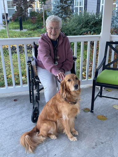 A senior woman sits on a porch with her golden retriever beside her, enjoying the outdoors.