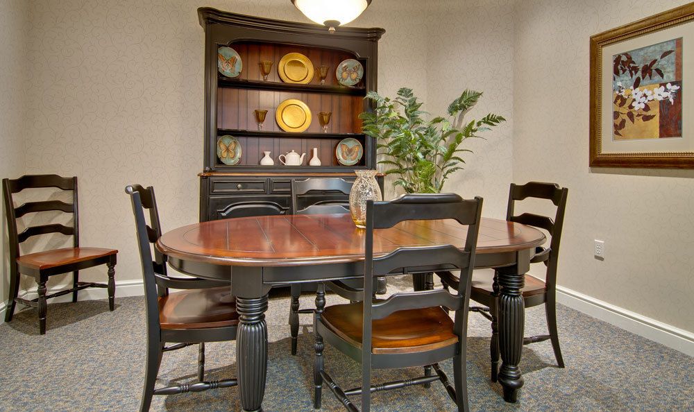 A cozy dining room featuring a wooden table with chairs, a decorative hutch, and a leafy plant centerpiece.