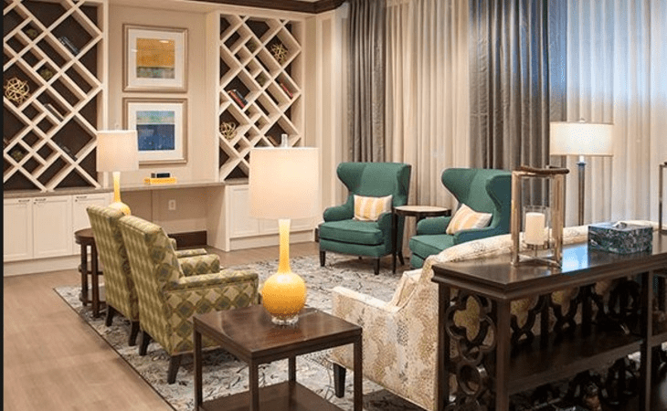 A cozy living room with elegant furniture, including chairs and a lamp, adorned with artwork and decorative shelving.