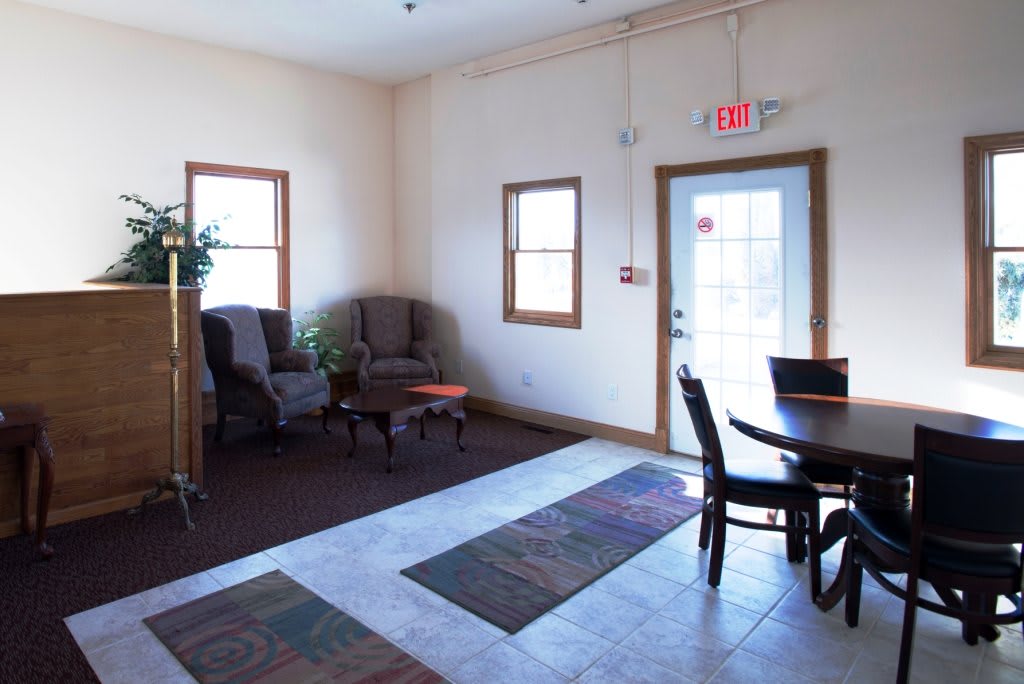 A cozy waiting room with chairs, a table, and a potted plant by the windows.