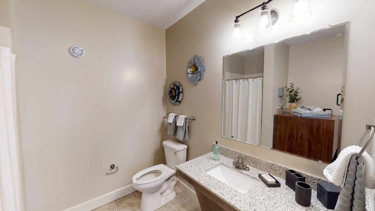 A clean and modern bathroom with a toilet, sink, mirror, and towels.