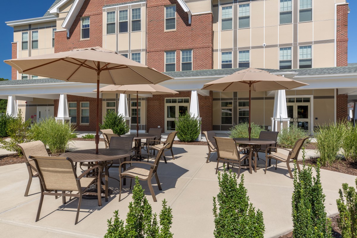 An outdoor patio area with tables, chairs, and umbrellas in front of a building.