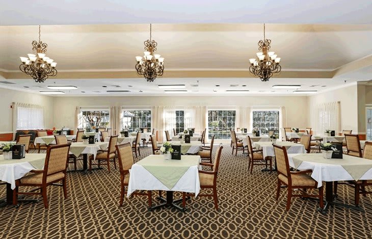 An elegant dining room with tables and chairs arranged neatly under ornate chandeliers.