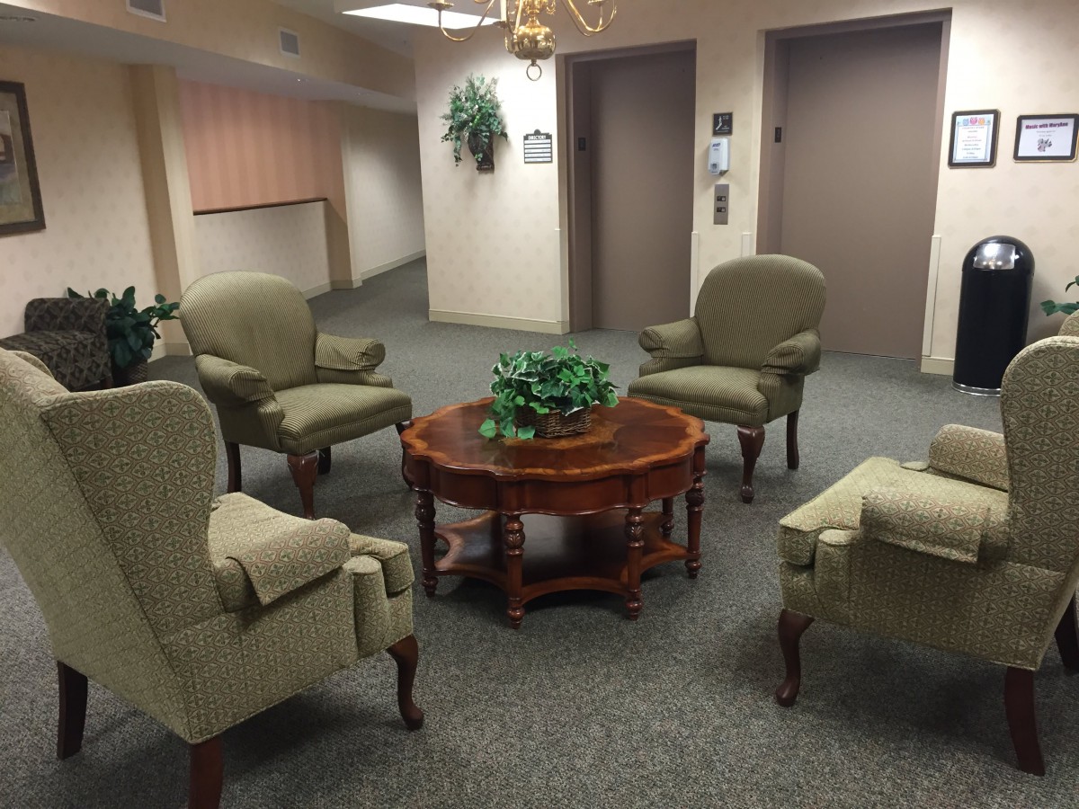 A cozy lobby with armchairs arranged around a wooden table near elevators.