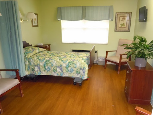 A cozy hospital room featuring a bed with colorful bedding, a chair, and natural light streaming through the window.