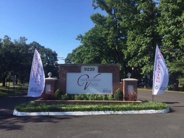 An outdoor entrance sign with banners on either side, surrounded by greenery and trees.