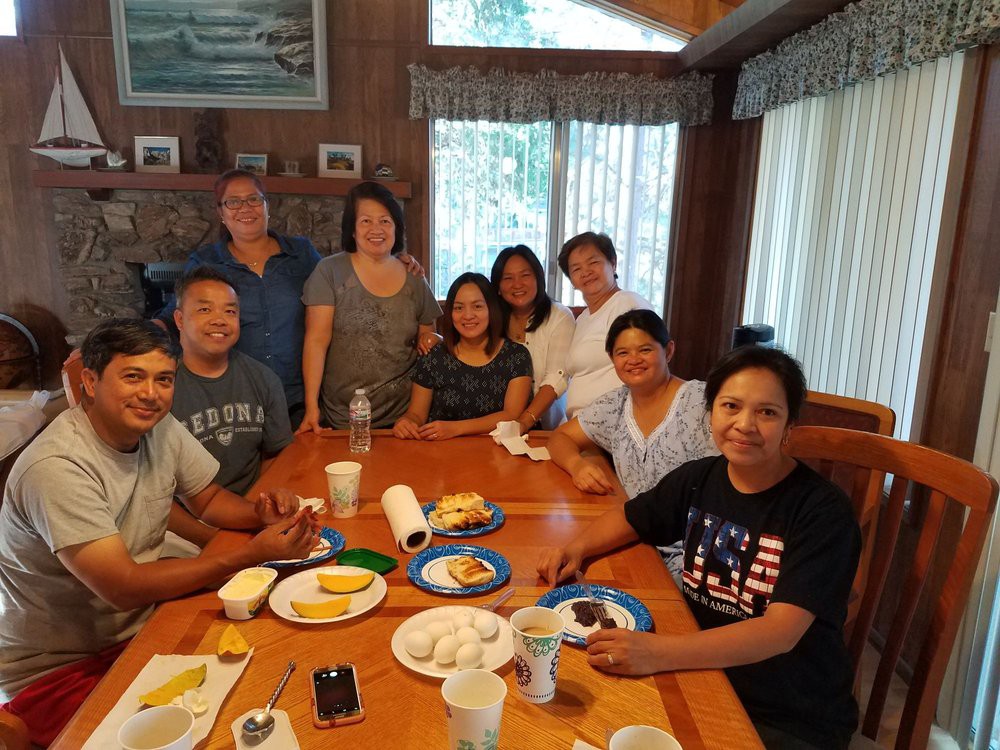 A group of people gathered around a dining table with food, enjoying a casual indoor meal.