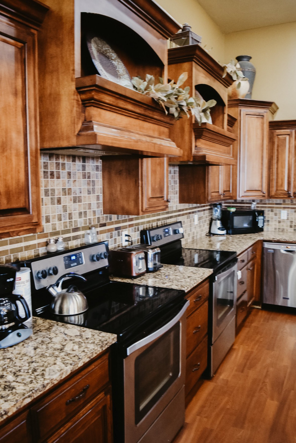 A modern kitchen with wooden cabinets, granite countertops, and various appliances including a stove, oven, microwave, and coffee maker.