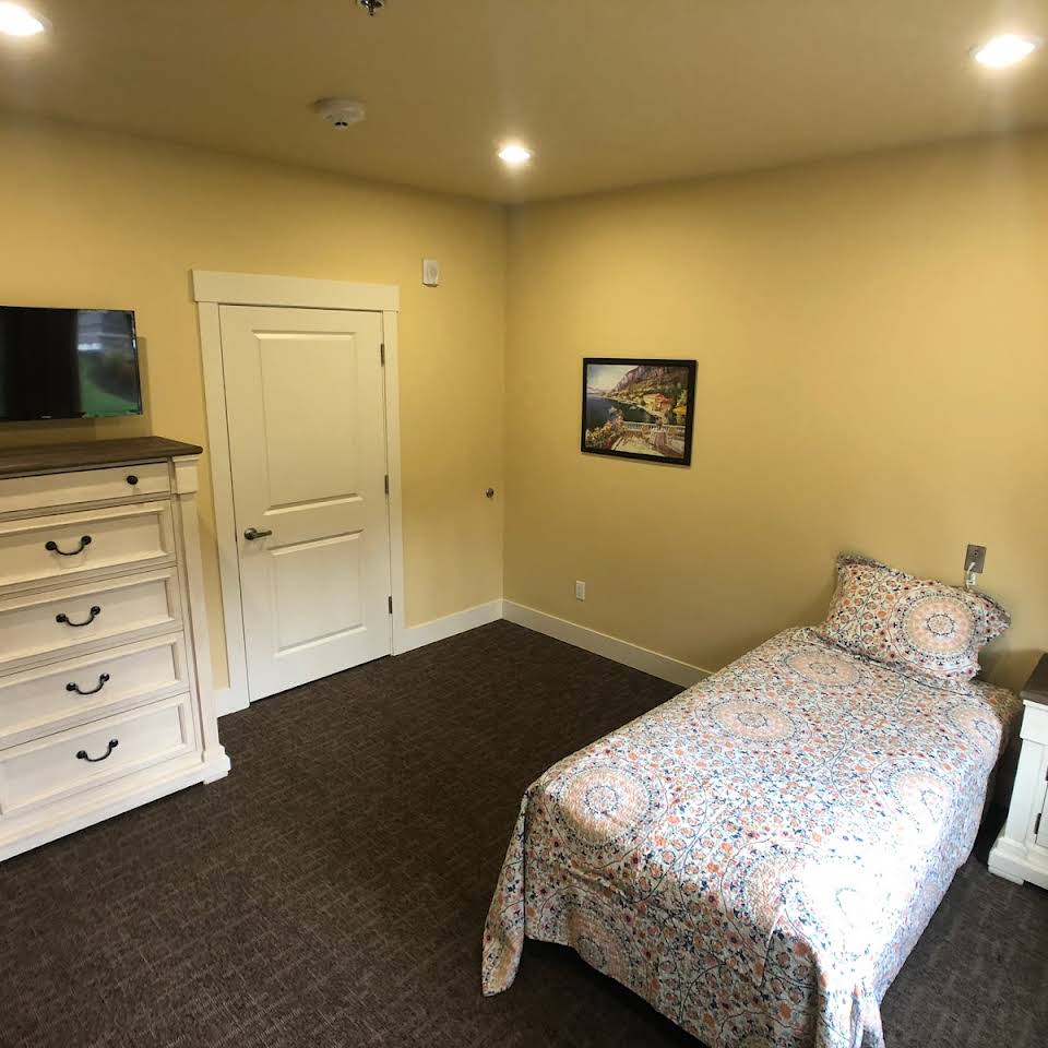 A simple bedroom with a single bed, dresser, and wall-mounted TV.