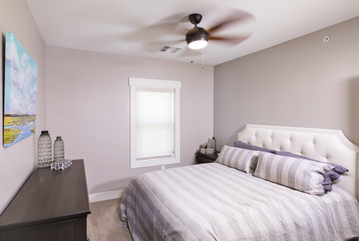 A minimalist bedroom with a neatly made bed, neutral color scheme, and a ceiling fan.