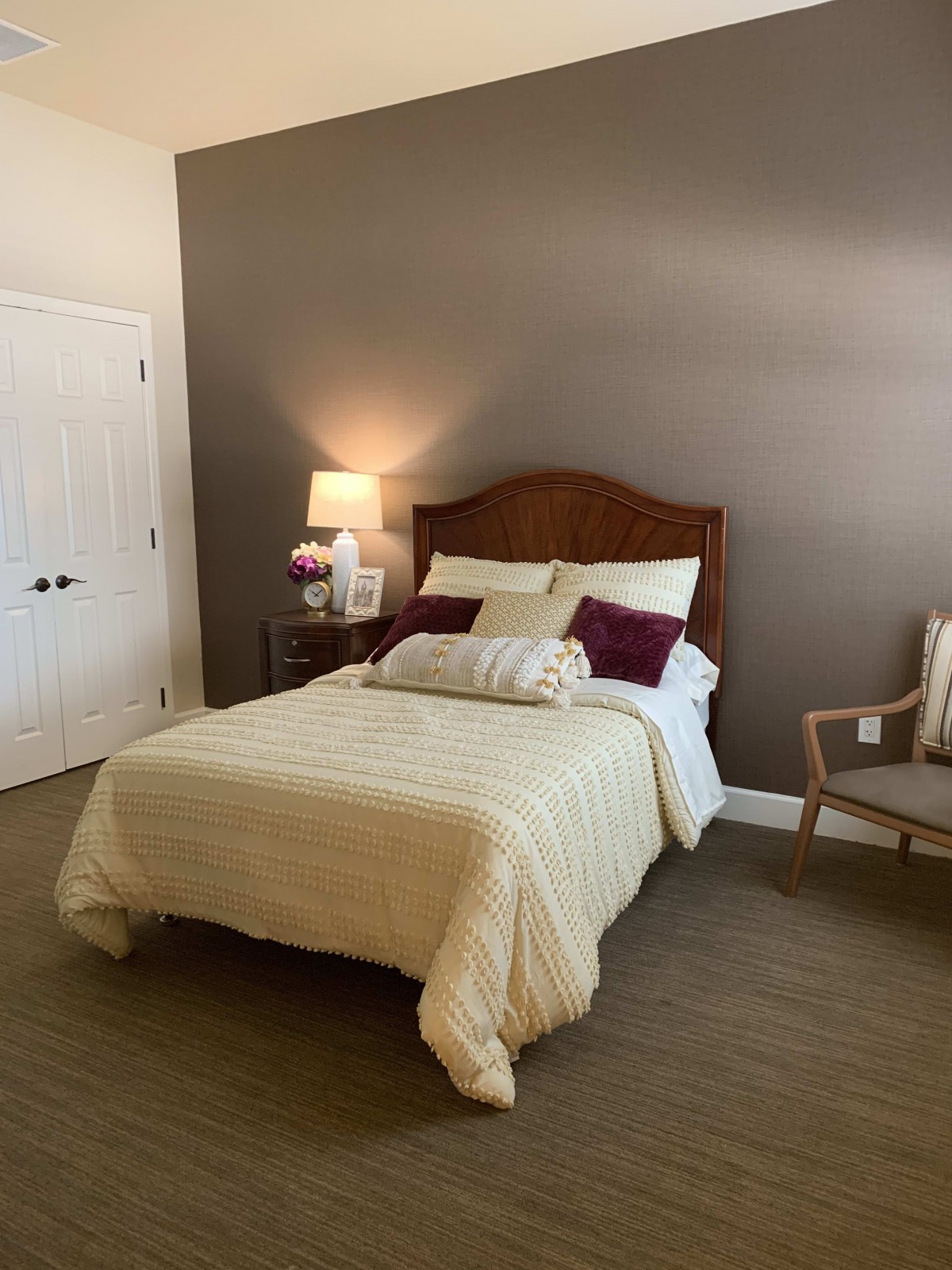 A cozy bedroom with a neatly made bed, decorative pillows, a bedside lamp, and an armchair.