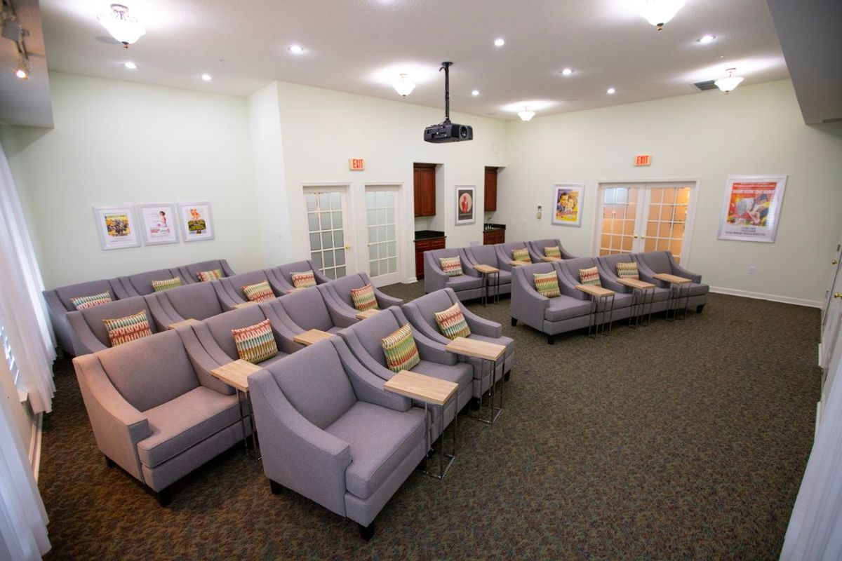 An auditorium room with multiple rows of comfortable chairs and a central projector.