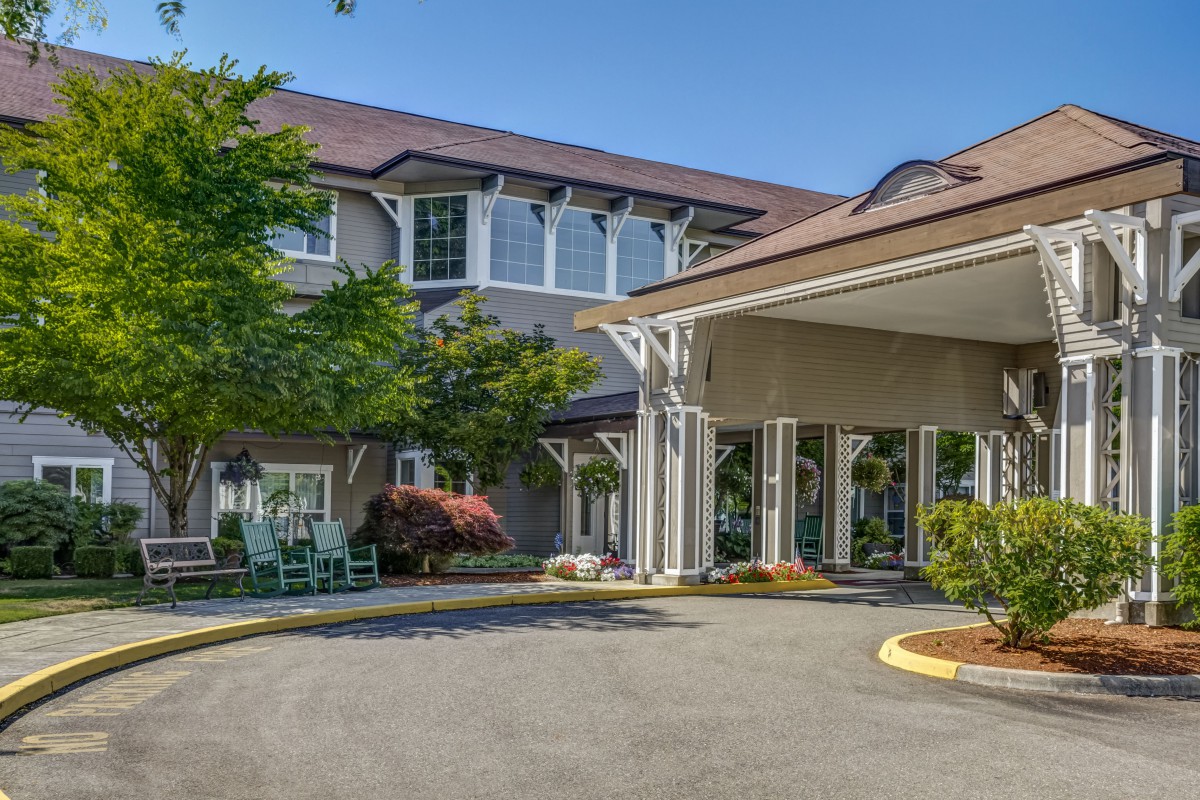 A well-maintained building entrance with surrounding greenery and a driveway.