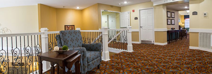 A cozy hotel lobby area with a patterned carpet, comfortable seating, and decorative railing.