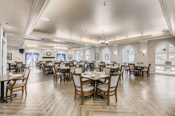 An elegantly designed dining area with multiple tables and chairs, featuring chandeliers and a wooden floor.