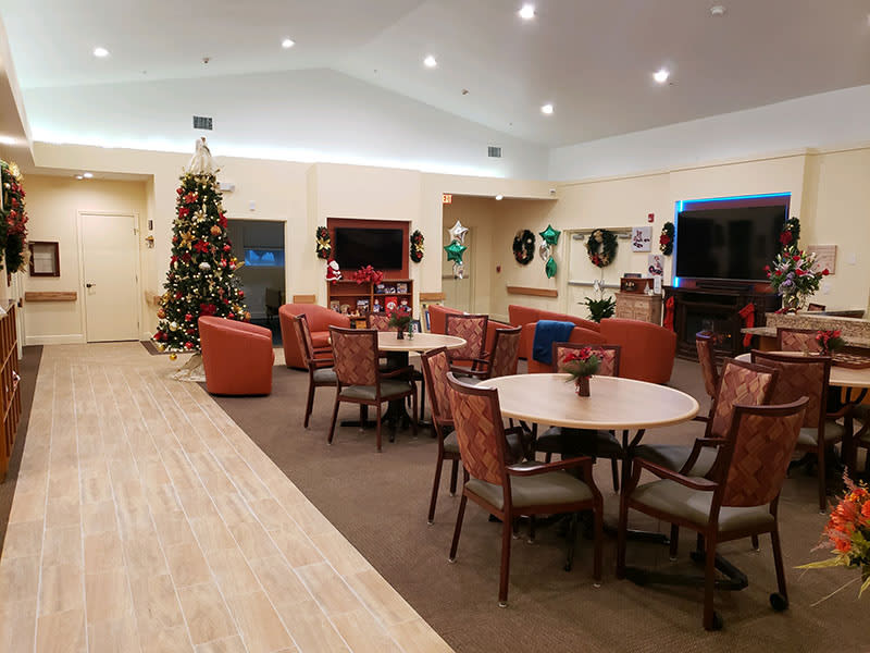 A cozy lounge area decorated with Christmas decorations, featuring tables and chairs, a television, and a festive tree.