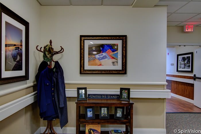 Office interior with a coat rack, framed artwork, and a shelf displaying photos.