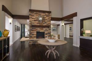 A modern living room with a central stone fireplace and wooden flooring.