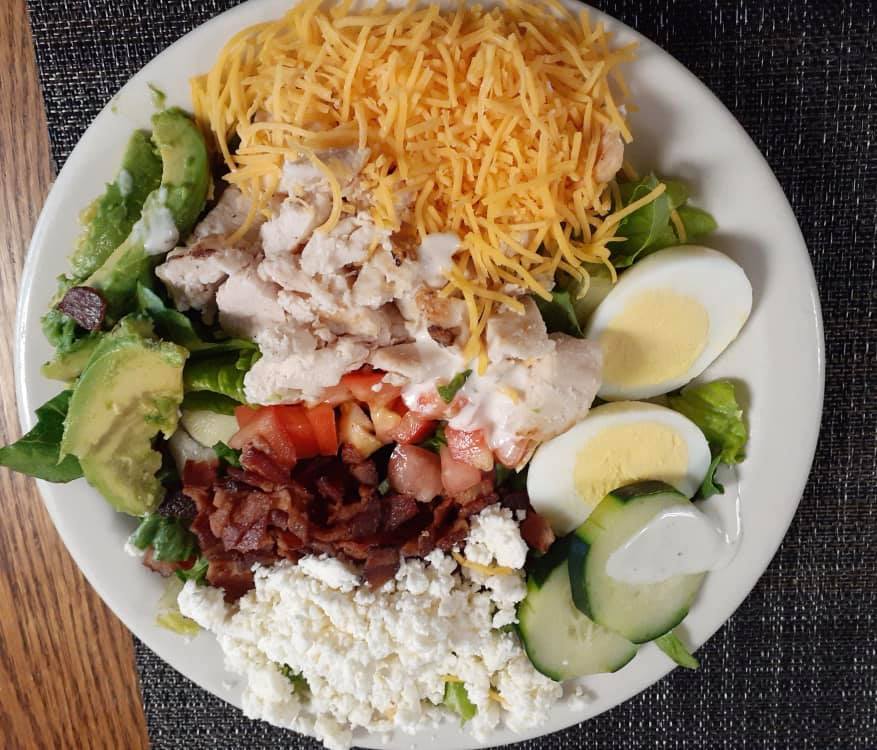 A fresh Cobb salad with various toppings including avocado, chicken, cheese, boiled egg, and bacon.