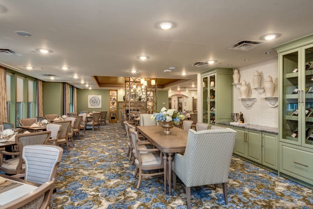 A spacious dining area with elegant chandeliers, floral carpet, and neatly arranged tables and chairs.