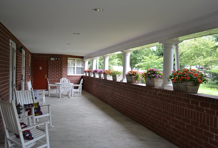 A peaceful porch with white chairs, flower pots, and a brick wall.