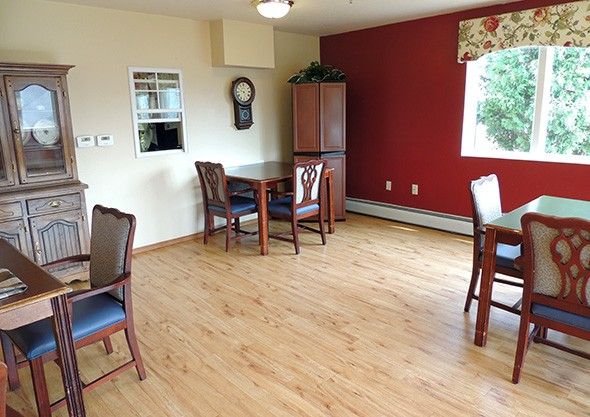 A cozy dining area with wooden floors, several tables and chairs, and a window letting in natural light.
