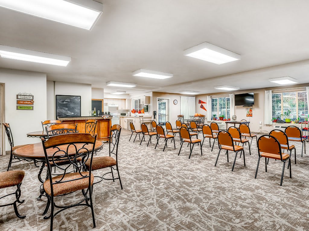 A spacious dining area with multiple tables and chairs, featuring a patterned carpet and modern ceiling lighting.
