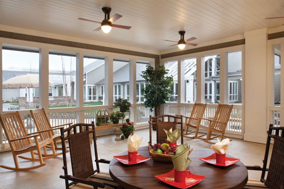 A cozy veranda with a dining area, rocking chairs, and large windows.