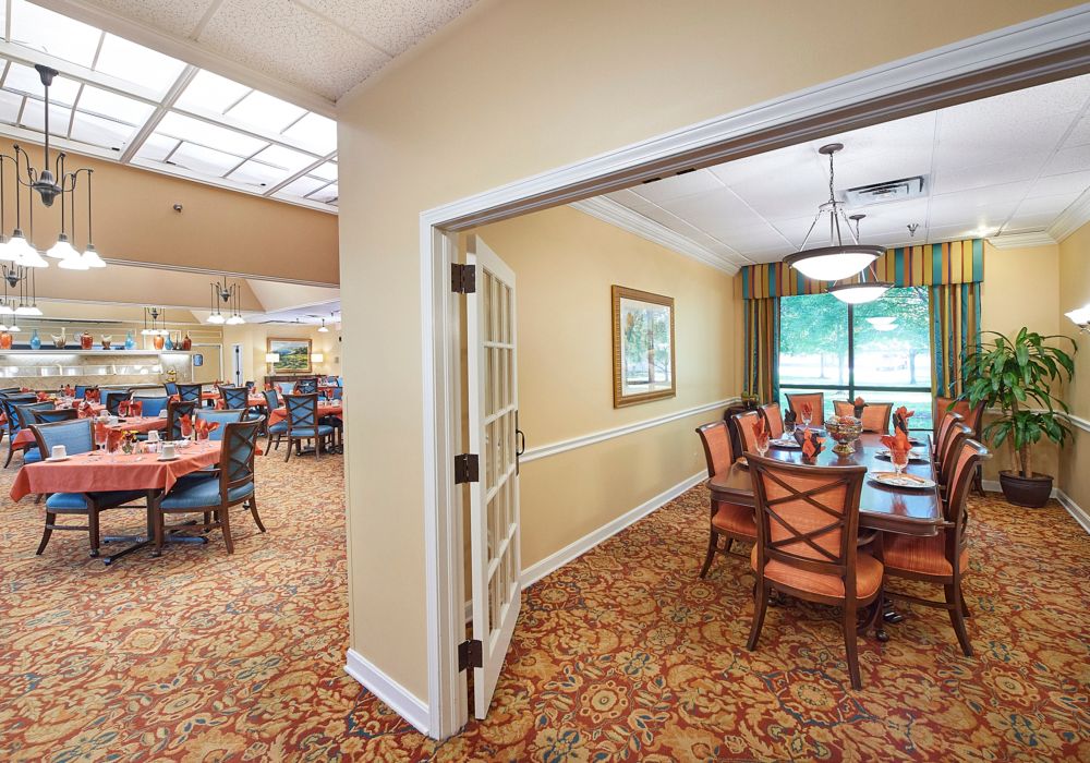A beautifully decorated dining area with a large table and chairs, featuring carpeted floors and natural lighting from a window.