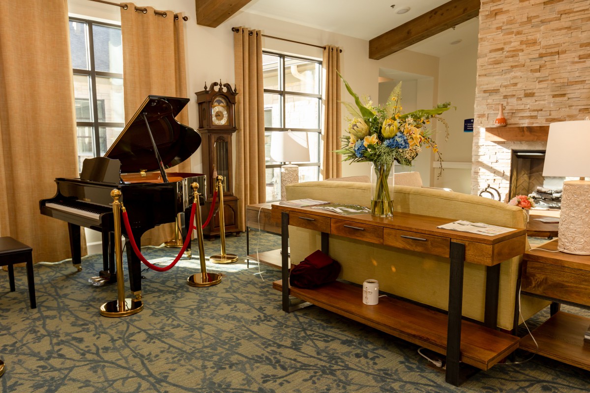 A cozy living room featuring a grand piano, grandfather clock, and elegant floral arrangement.