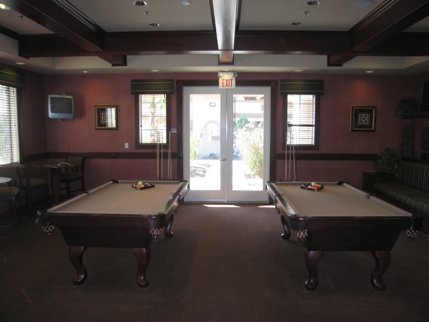 A cozy billiard room featuring two pool tables and natural lighting from windows.