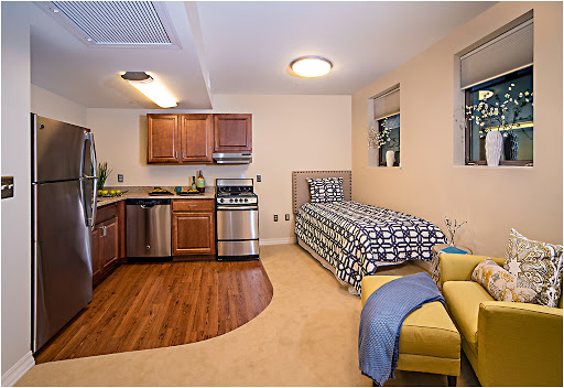 A cozy studio apartment featuring a kitchen area and a single bed, designed for efficient living.