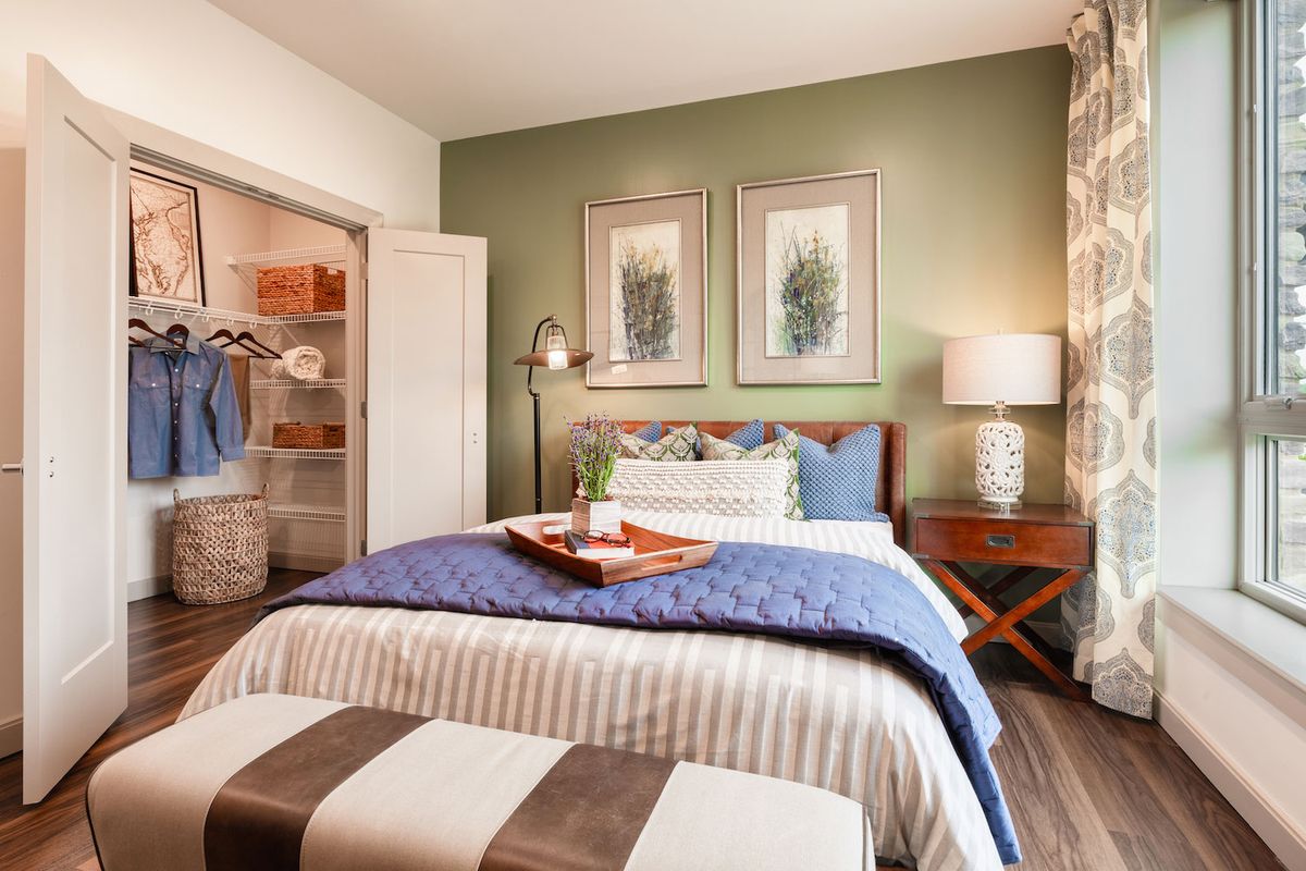 A cozy and modern bedroom with green walls, stylish artwork, and a neatly made bed.