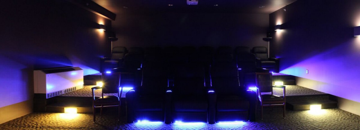 A dimly lit home theater with blue accent lighting illuminating the seating.